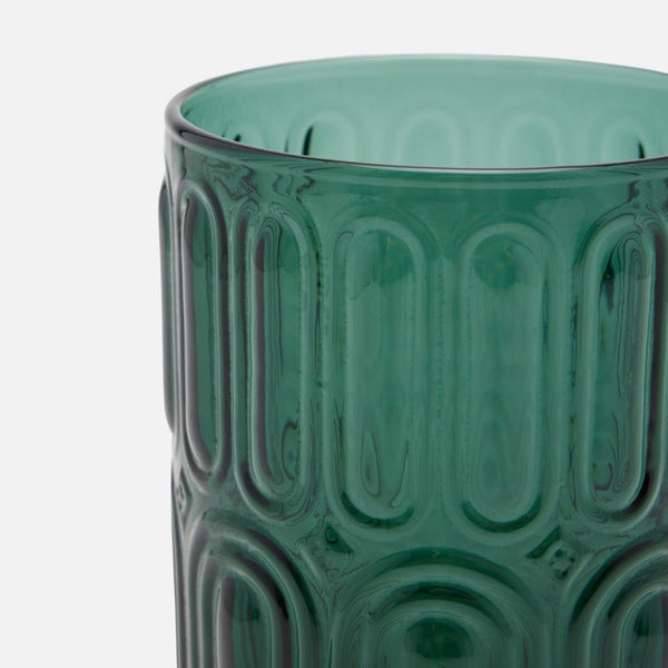 A close-up of a translucent teal green glass highball with a vertically ribbed, oval-patterned design, set against a plain light gray background.