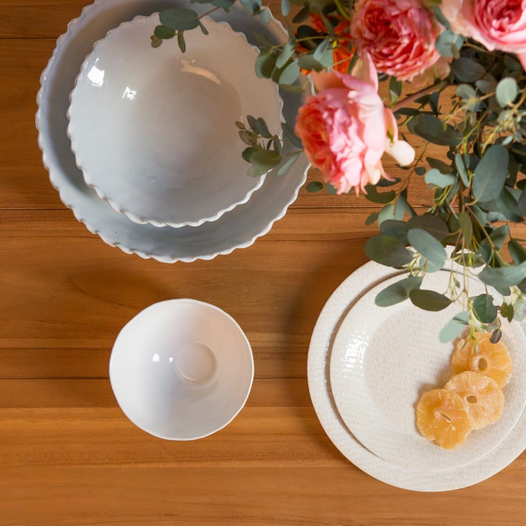 White ceramic bowls and a plate with flowers and fruit on a wooden surface