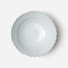 A top-down view of a scalloped ceramic bowl with a light gray glaze, set against a plain white background.