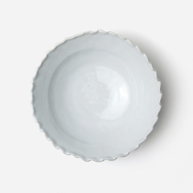 A top-down view of a scalloped ceramic bowl with a light gray glaze, set against a plain white background.