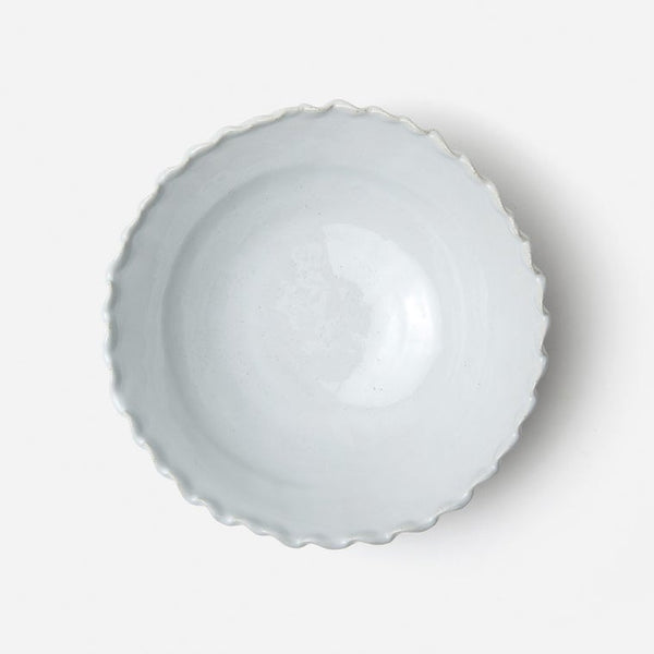 A top-down view of a scalloped ceramic bowl with a light gray glaze, set against a plain white background.
