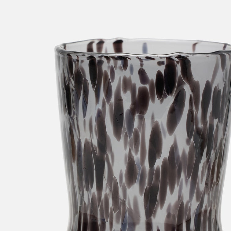 A close-up of a textured glass carafe or cup with a dark gray and black spotted pattern on a white background.