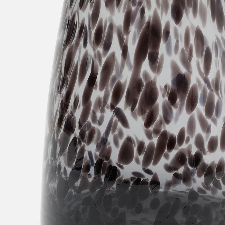 Close-up of a glossy glass carafe with a dark brown and black spotted pattern on a clear glass background, set against a plain white studio backdrop.