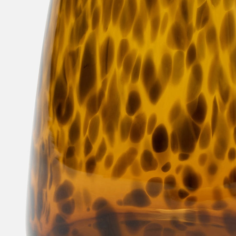 Close-up of a glossy amber glass object with a dark brown mottled or leopard-like pattern, photographed against a plain white background.