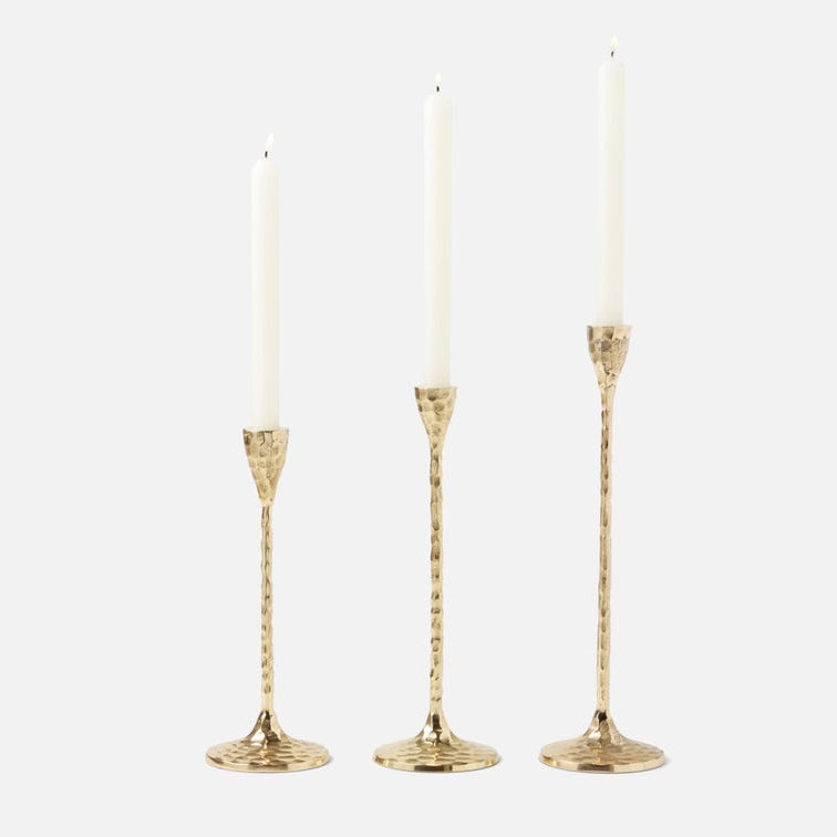 Three gold candlestick holders with textured stems and white taper candles, arranged against a light gray background.