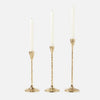 Three gold candlestick holders with textured stems and white taper candles, arranged against a light gray background.