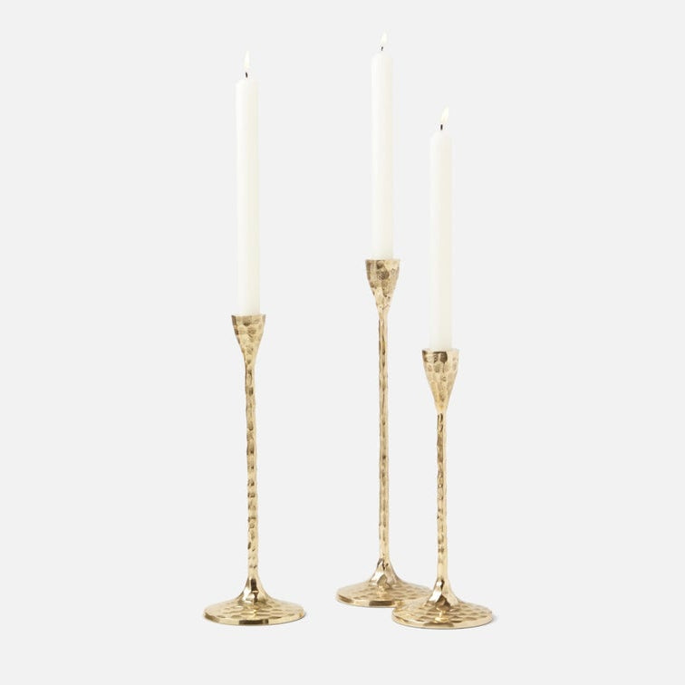 Three gold candlestick holders with textured stems and round bases, each holding a white taper candle, photographed on a light gray background.