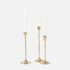 Three gold candlestick holders with textured stems and round bases, each holding a white taper candle, photographed on a light gray background.