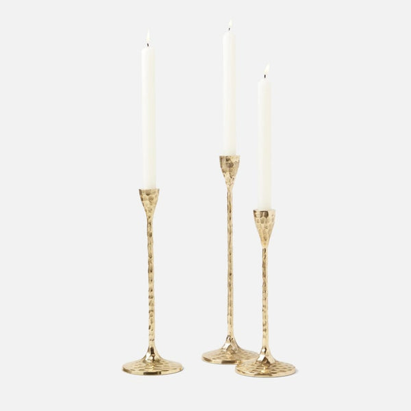 Three gold candlestick holders with textured stems and round bases, each holding a white taper candle, photographed on a light gray background.