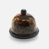 A small glossy dome-shaped serving piece with a rounded top and circular base, featuring a tortoiseshell pattern in amber, brown, and black on a plain white background.