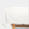A white tablecloth draped over a wooden table, shown against a plain white background.