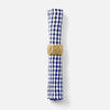 A rolled napkin with a blue and white gingham check pattern, secured with a textured gold ring, shown against a light gray background.