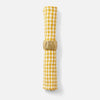 A rolled yellow and white gingham check linen napkin held by a textured gold metal ring, set against a clean white background.