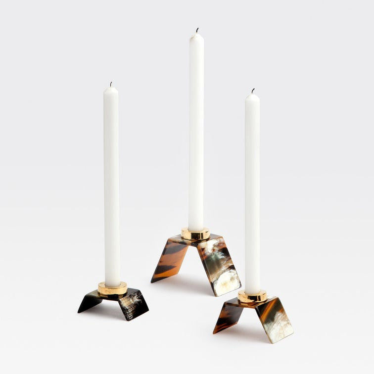 Three taper candle holders with white candles, featuring tortoiseshell-patterned bases in black, brown, and cream, accented with gold-tone metal rings, set against a light gray background.