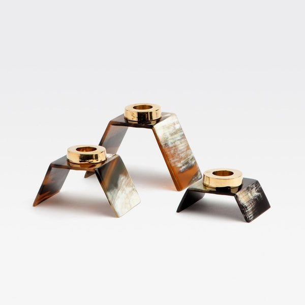 Three modern V-shaped candle holders made of tortoiseshell with polished gold-tone metal tops, arranged on a light gray background.