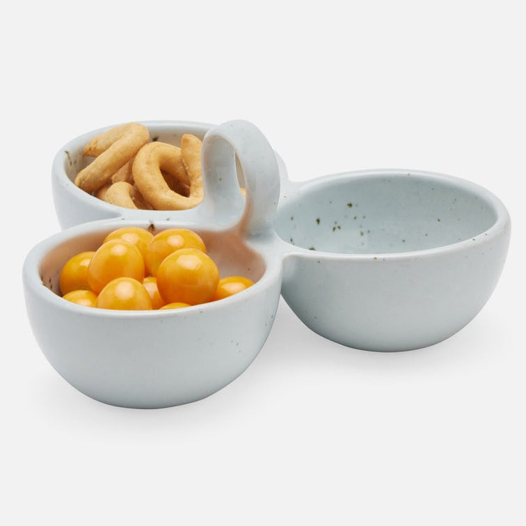 A three-compartment stoneware snack bowl in a pale blue-gray glaze, shown on a clean white background. The left compartment holds golden-brown ring-shaped snacks, the bottom-left compartment holds bright yellow round snacks, and the right compartment is empty.