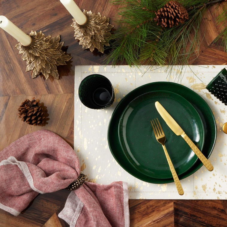 Christmas-themed table setting with green plates, gold cutlery, and pinecones on a wooden table.
