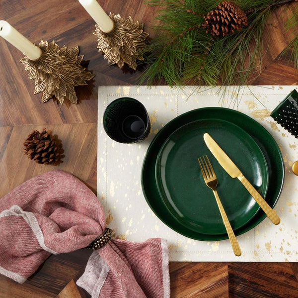 Christmas-themed table setting with green plates, gold cutlery, and pinecones on a wooden table.