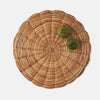 A round, hand-woven natural fiber placemat in a light tan color, styled with two small green apples on a solid light gray background.