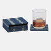 A set of navy blue and white ikat patterned coasters, including one coaster holding a clear textured tumbler glass with an amber drink and an ice cube, shown on a light gray background.