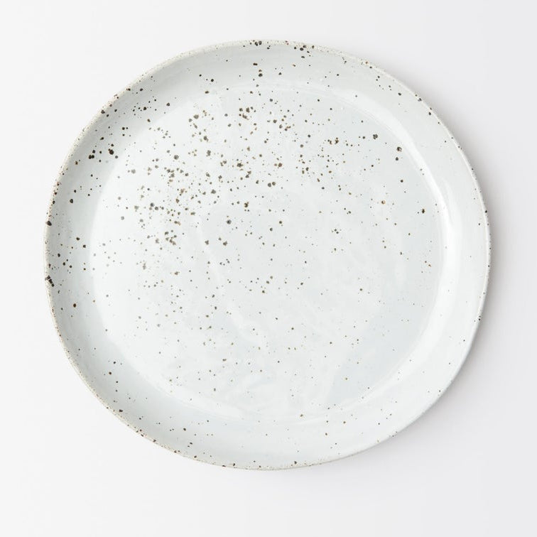 A round white stoneware plate with a rustic hand-painted finish and dark brown speckles, photographed from directly above on a clean white background.