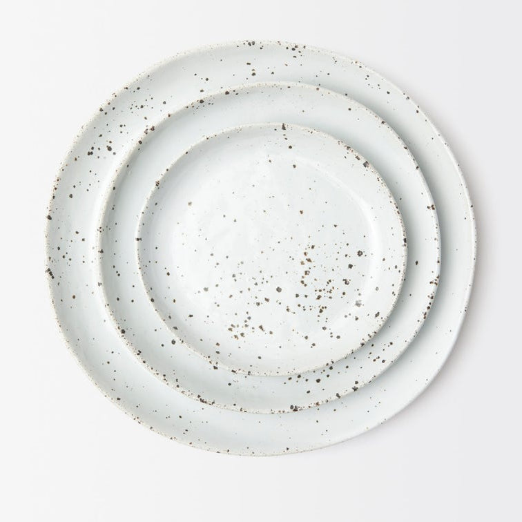 Three nested stonware plates in white with dark brown speckled detailing, photographed from directly above on a clean white background.