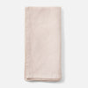 A folded light blush pink linen napkin with decorative hand-stitched borders, shown on a clean white background.