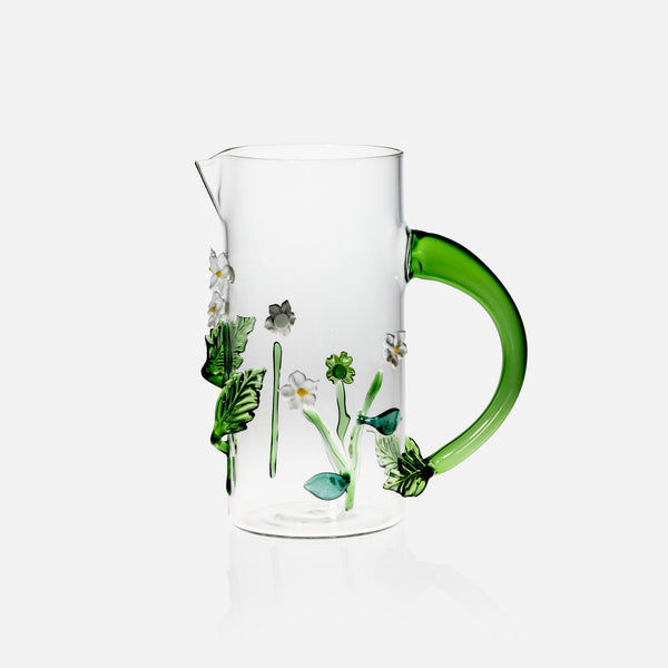Clear glass pitcher with green handle and floral design on a white background