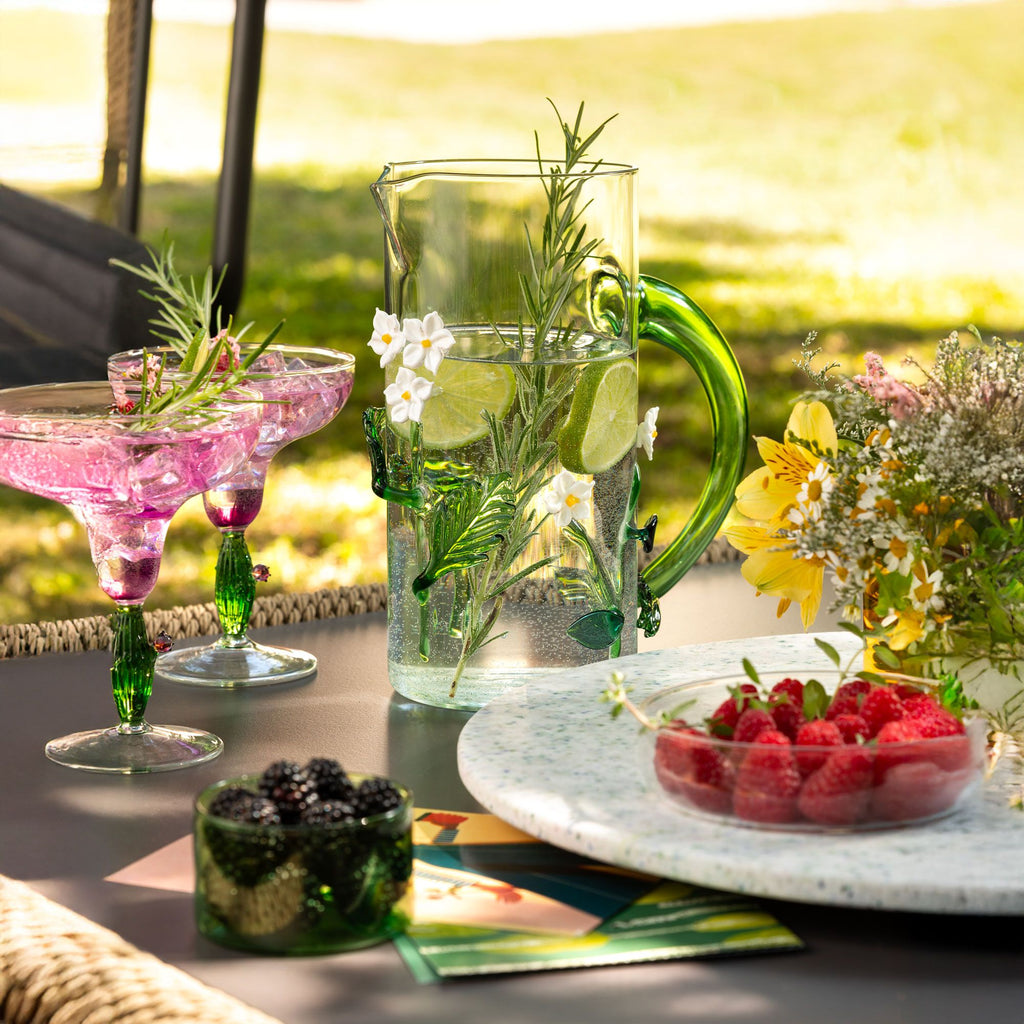 Outdoor setting with cocktails, a pitcher of water, and a bowl of raspberries on a table.