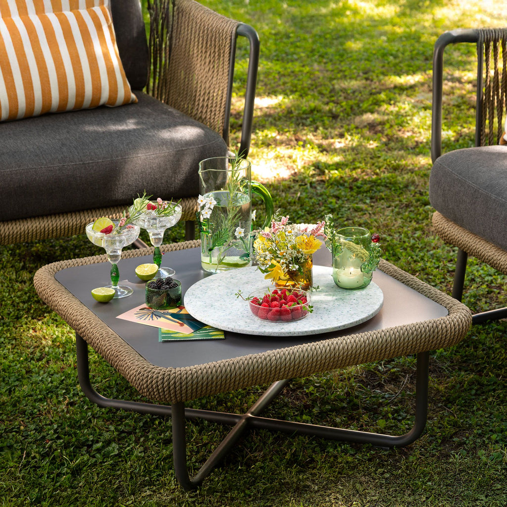 Outdoor setting with a coffee table, chairs, and decorative items on a grassy area