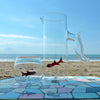 Clear glass pitcher with fish on a mosaic table by the beach