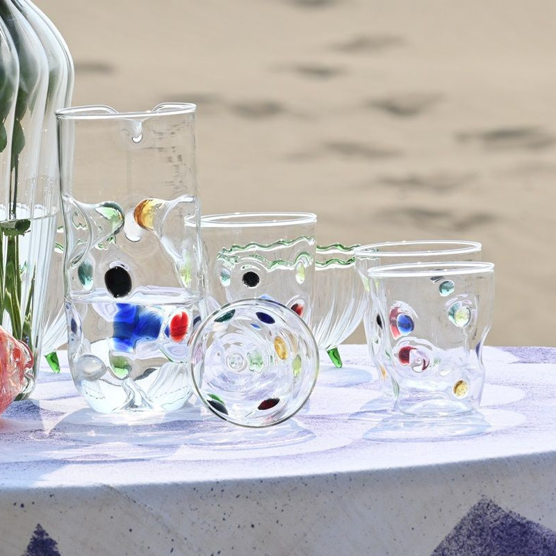 Collection of glass art pieces including vases and a fish-shaped object on a white surface with a blurred natural background.