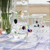 Colorful glass fish and a red glass bottle on a checkered tablecloth with a blurred natural background