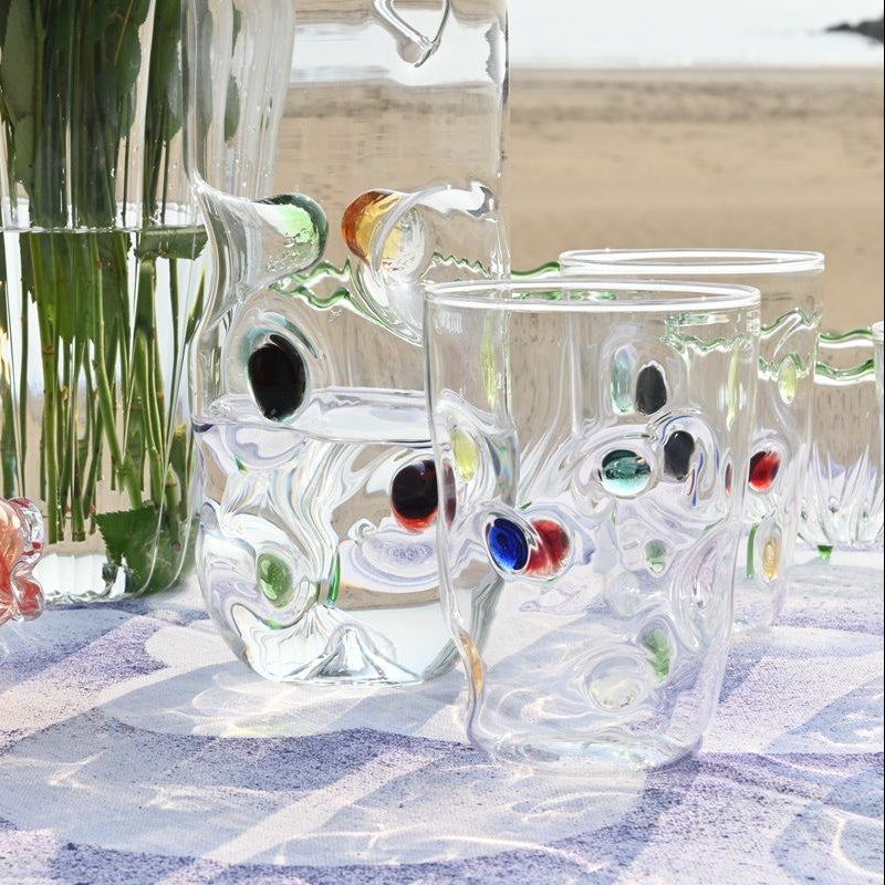 Colorful glass fish and a red glass bottle on a checkered tablecloth with a blurred natural background