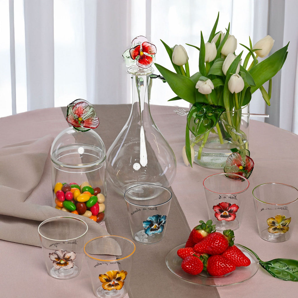 Decorative glassware with floral designs on a table with strawberries and candies.