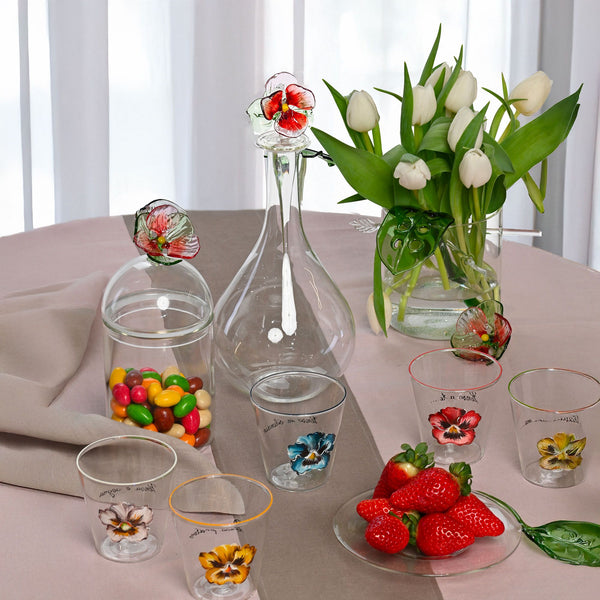 Decorative glassware with floral designs on a table with strawberries and candies.