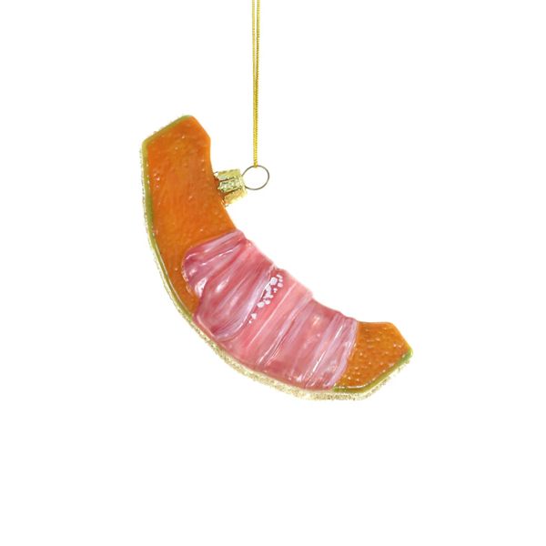 A slice of cantaloupe-shaped glass ornament featuring pink prosciutto wrapped design and gold glitter border  and a gold hanging string.