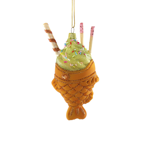 A decorative hanging ornament shaped like a fish-shaped waffle holding a green glittery ice cream swirl with sprinkles and two striped straws, shown on a plain white background.