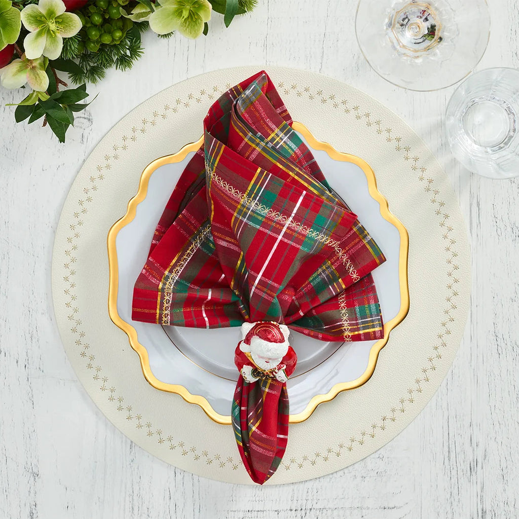 Plaid napkin with Santa Claus decoration on a white plate with gold rim, set against a festive background.