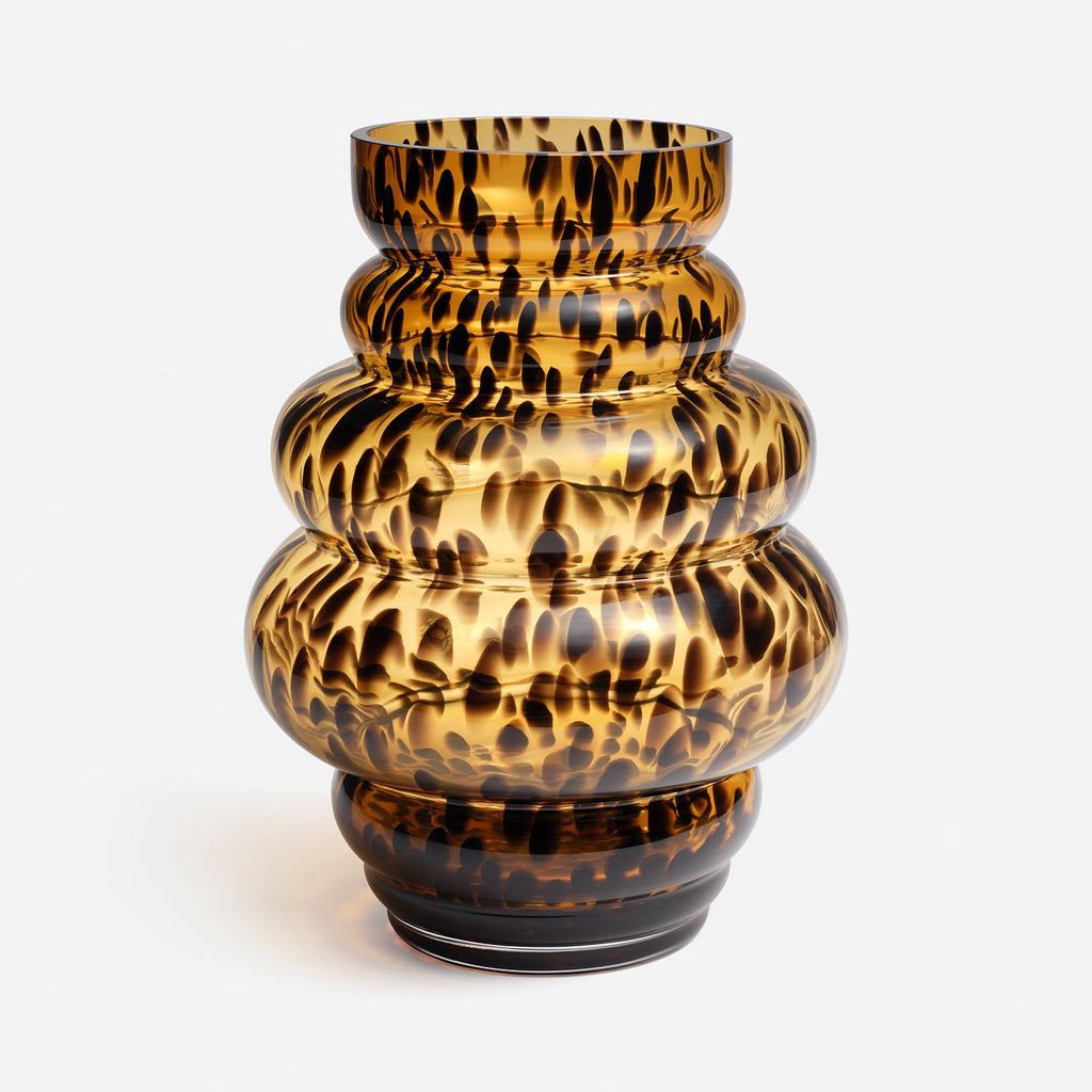 A sculptural, ribbed glass vase with a glossy amber-brown and black tortoiseshell pattern, set against a plain light gray background.