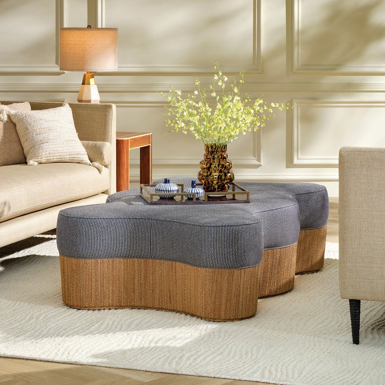 One wavy-shaped ottoman with gray ribbed fabric tops and natural woven bases, styled in a bright living room with a sofa, lamp, and vase of flowers.