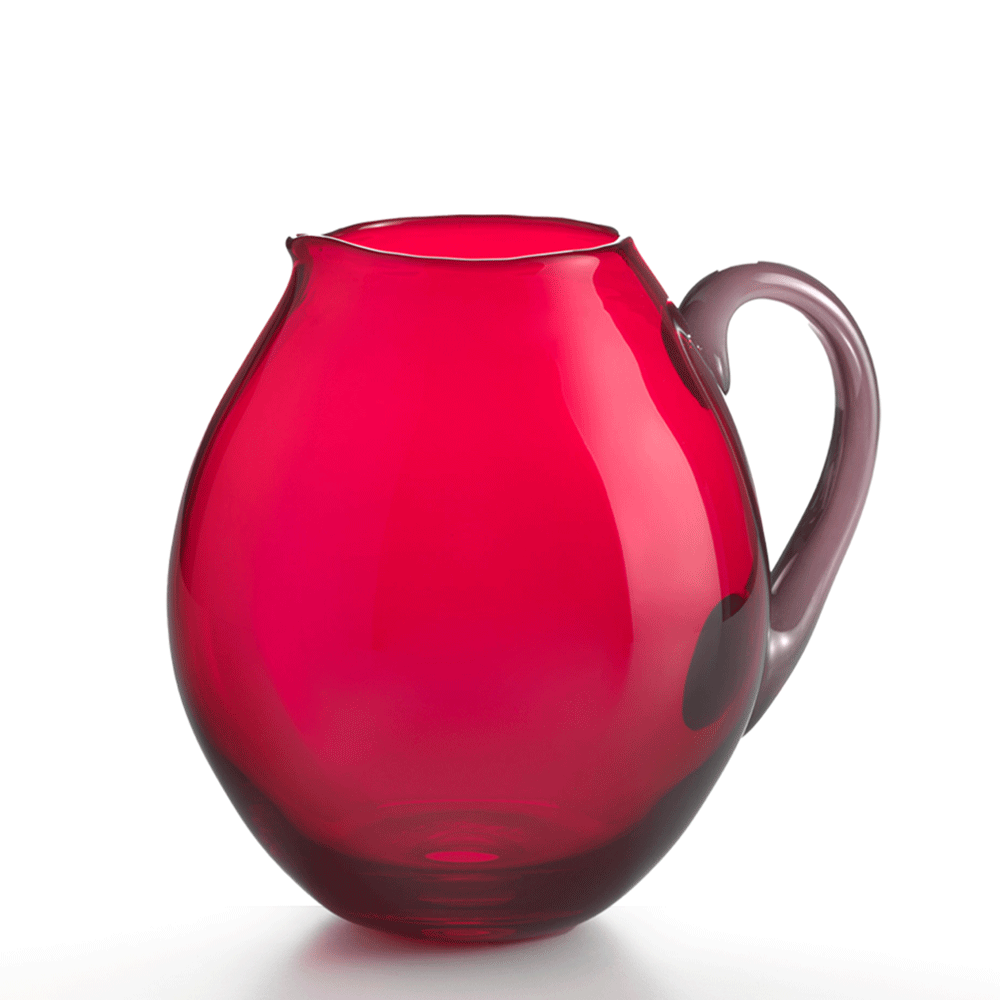 Red glass pitcher with taupe silver handle on flat white background