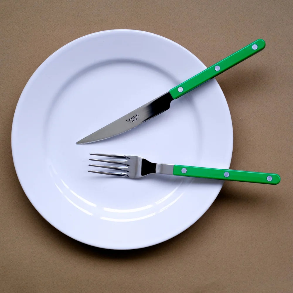A white ceramic plate on a brown background, holding a green-handled knife and matching fork.