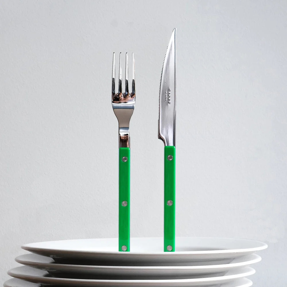 A fork and knife with bright green handles and silver metal heads, standing upright on a stack of white plates against a light gray background.