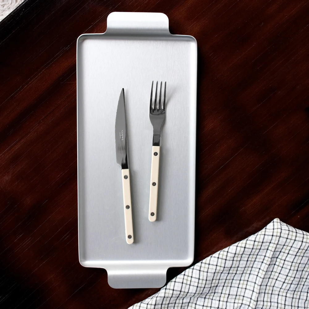 Silver knife and fork set on a gray rectangular plate with a wooden surface and checkered cloth in the background.