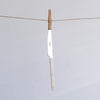 A single kitchen knife with a silver blade and a light beige handle is hanging from a wooden clothespin on a horizontal string against a plain light gray background.