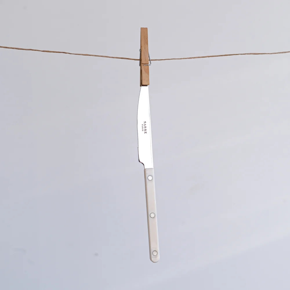 A single kitchen knife with a silver blade and a light beige handle is hanging from a wooden clothespin on a horizontal string against a plain light gray background.