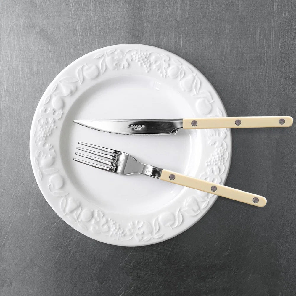 White decorative plate with silver knife and fork on a gray surface