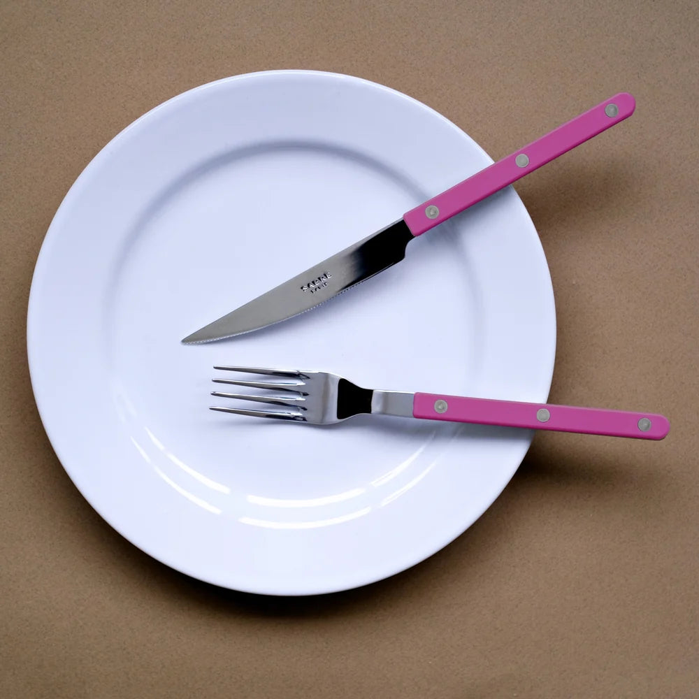 White plate with pink-handled knife and fork on a brown background