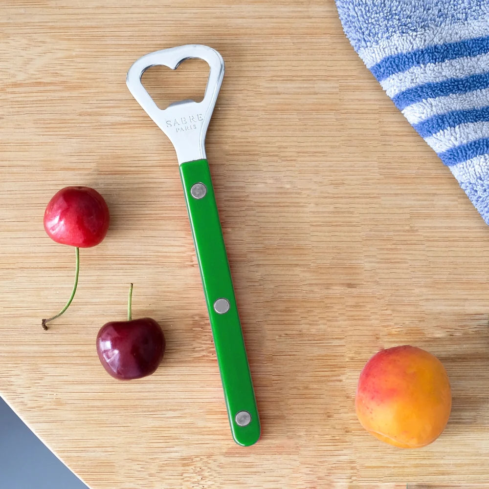 Green bottle opener with a hole on a wooden surface with cherries and an apricot.
